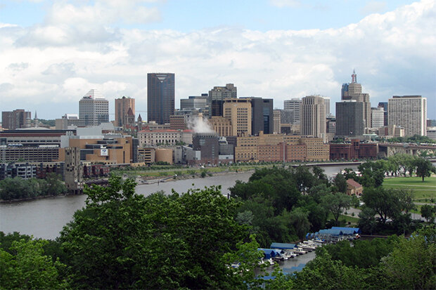 Trees, green space, and river in foreground, urban buildings in background